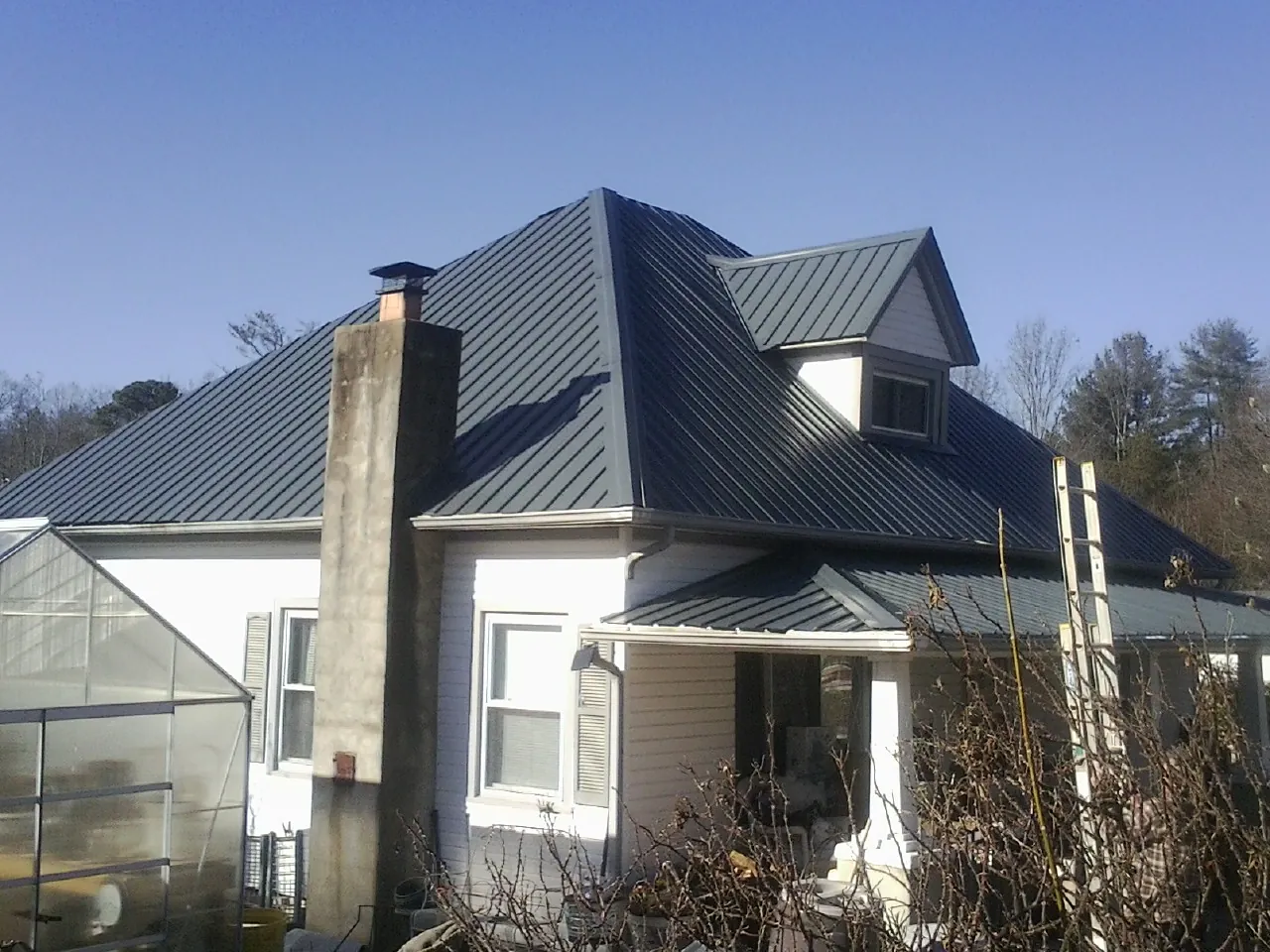 Dark blue standing seam metal roof on a white farmhouse with dormer — Slate & Tile Roof Repair by Roofing Brothers in Polo