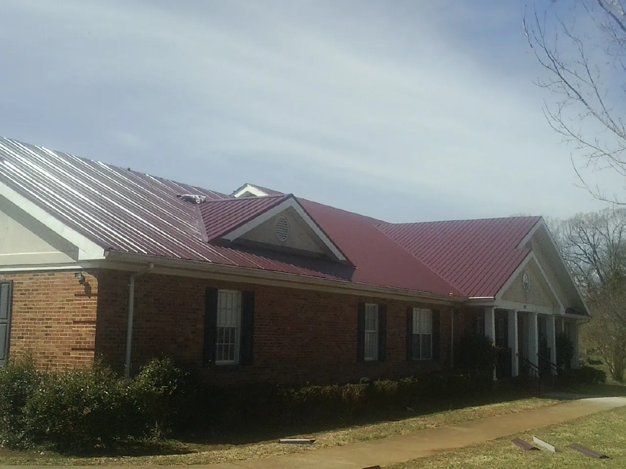 Red metal roof with gabled entries on a long brick building, from a Hail Damage Roof Repair job in Polo
