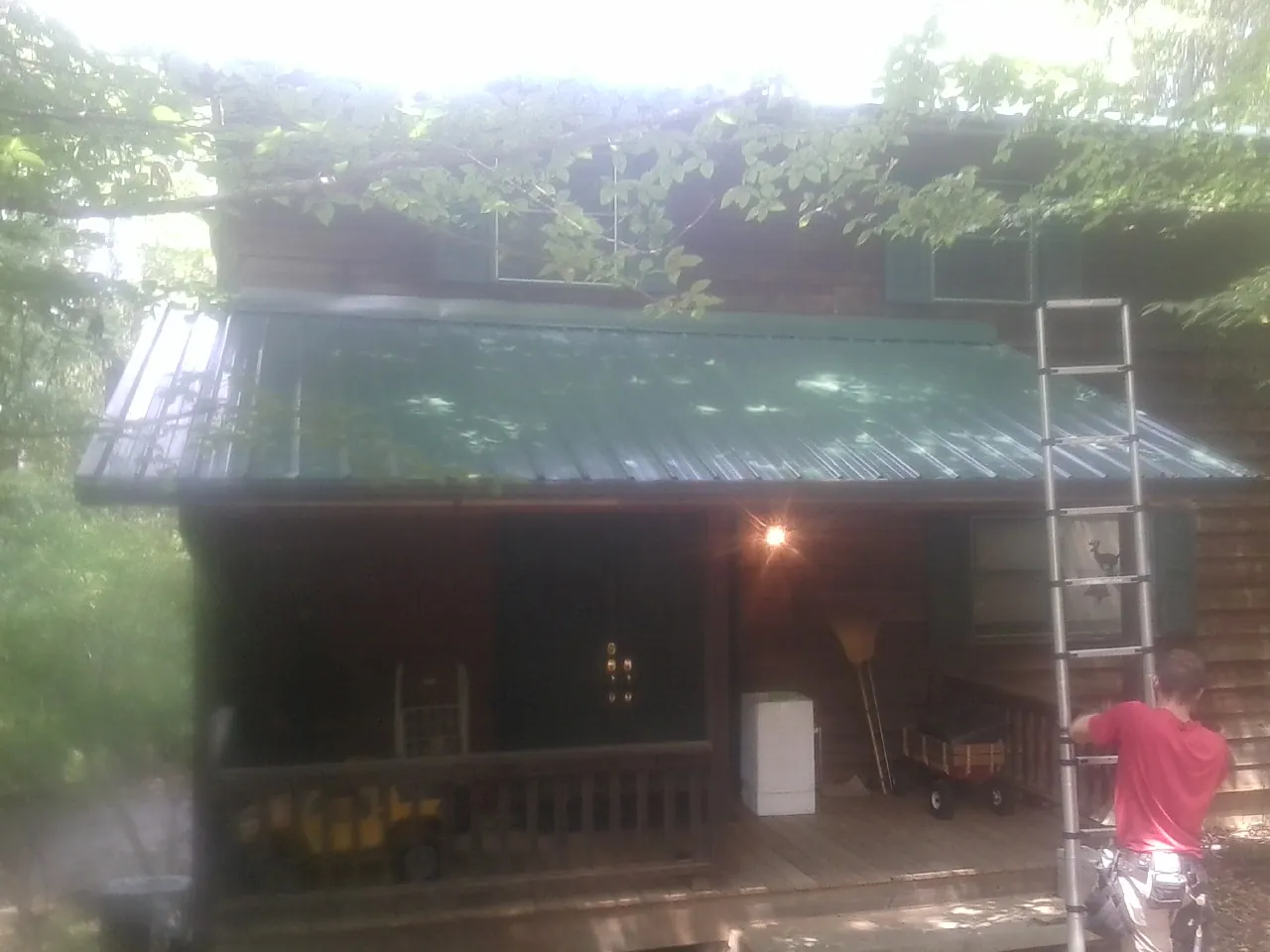 Worker on a ladder at the green porch roof of a wooded cabin in Polo