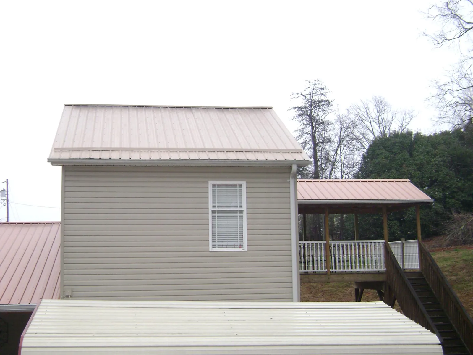 Tan metal roofs on a two story addition and attached porch, from a Roof Replacement job in Polo